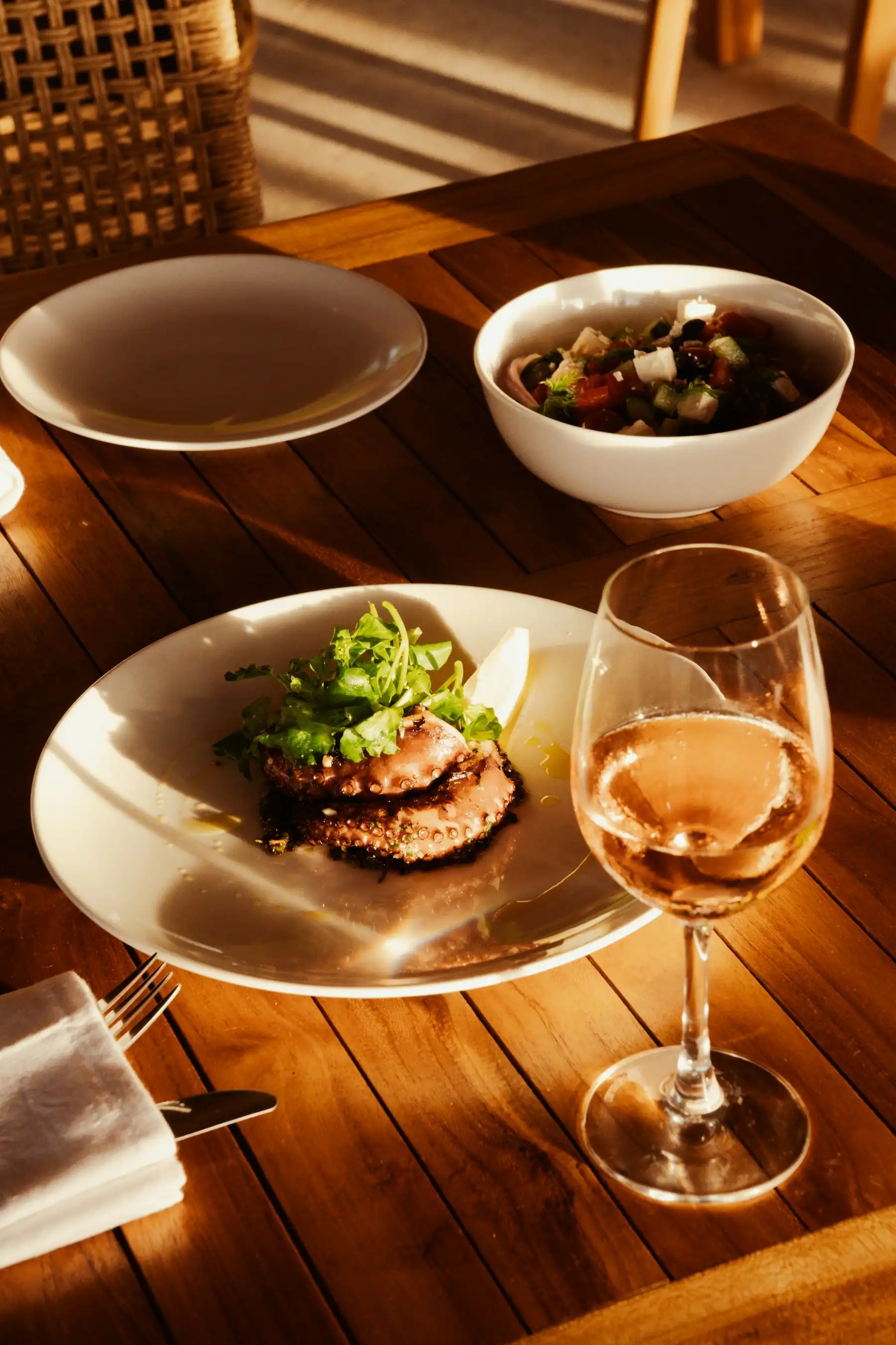 Grilled octopus, Greek salad and a glass of rosé on a sunlit vineyard-restaurant table