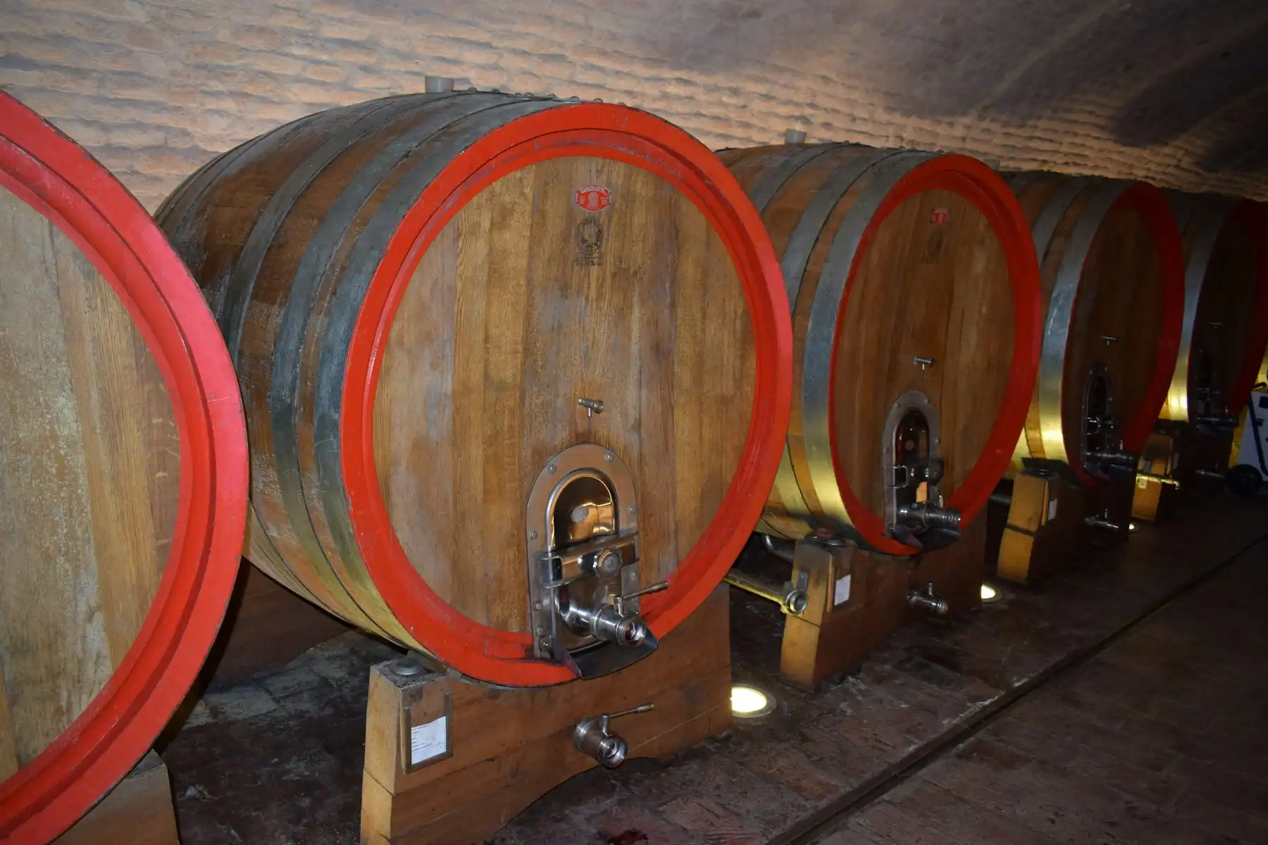 Old wooden casks with red-painted rims lined up in a low vaulted cellar