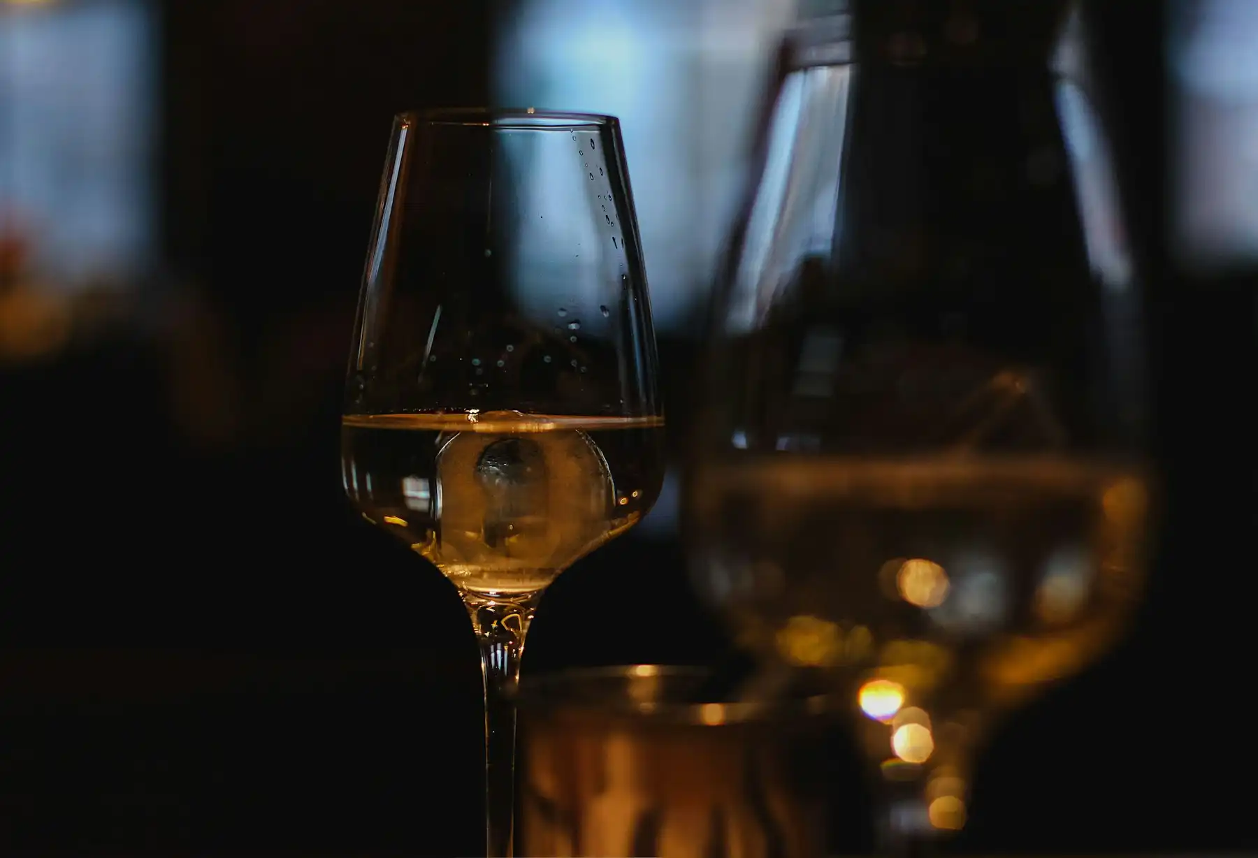 Two glasses of amber dessert wine backlit in a dark tasting room