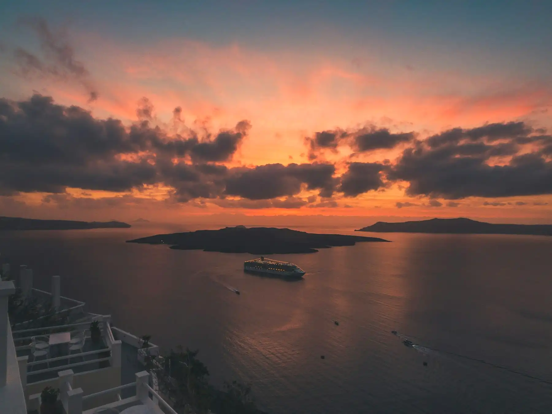 The caldera at dusk from a Fira balcony — an illuminated cruise ship and small boats on still water
