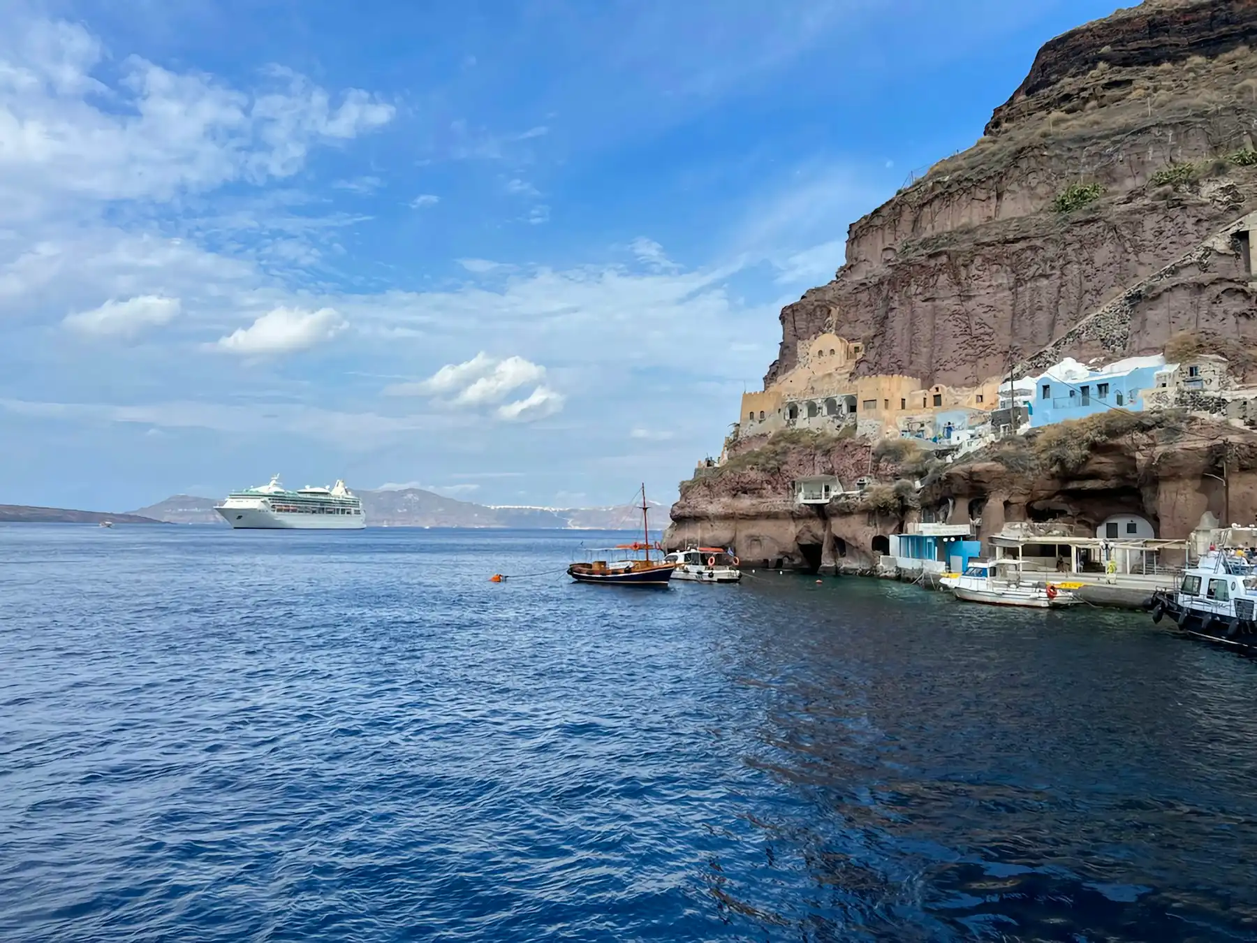 A cruise ship at anchor in the caldera beside the cliffs and cave houses of Fira’s old port