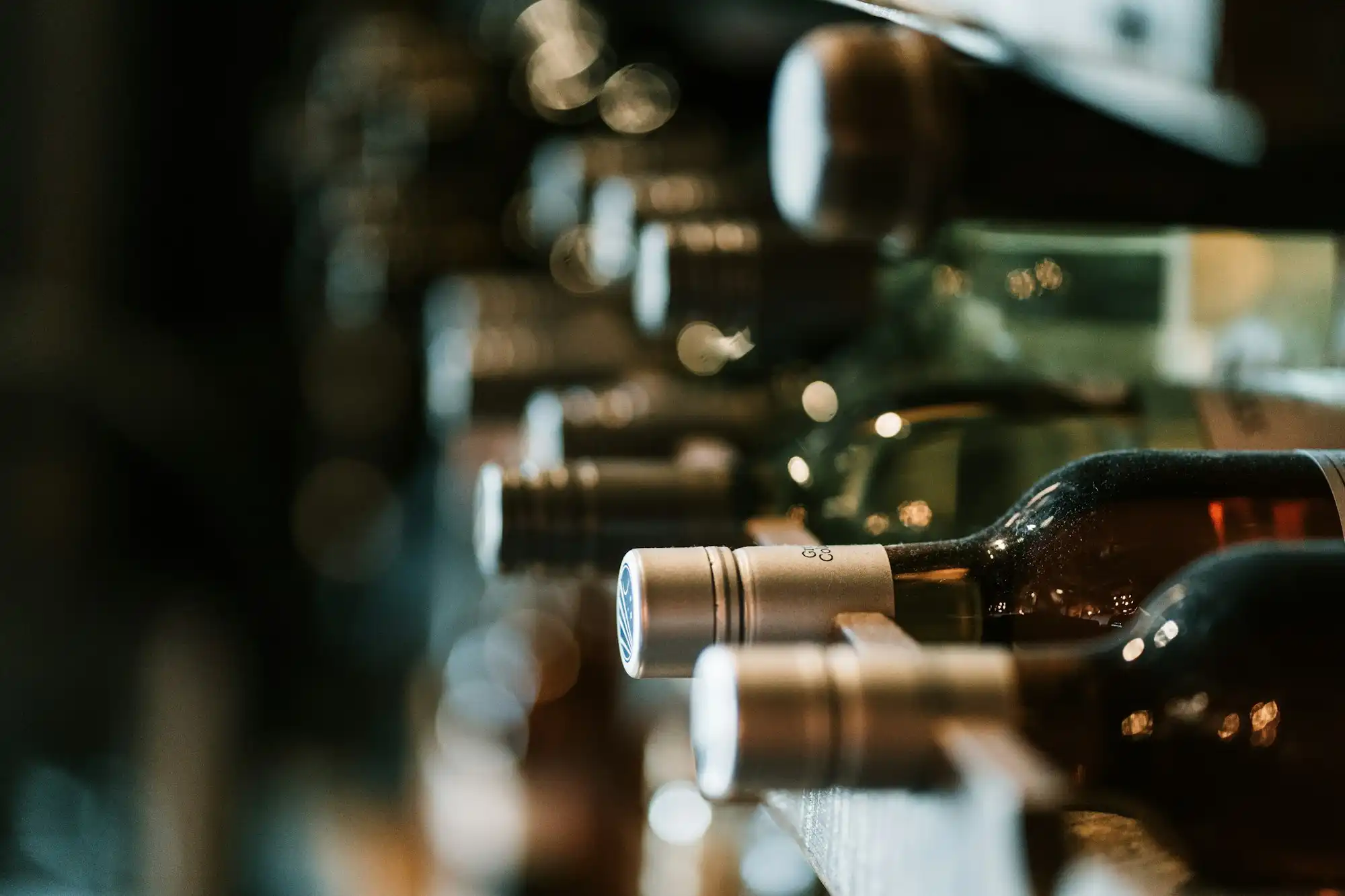 Wine bottles resting in a dim cellar rack, foil capsules catching the light