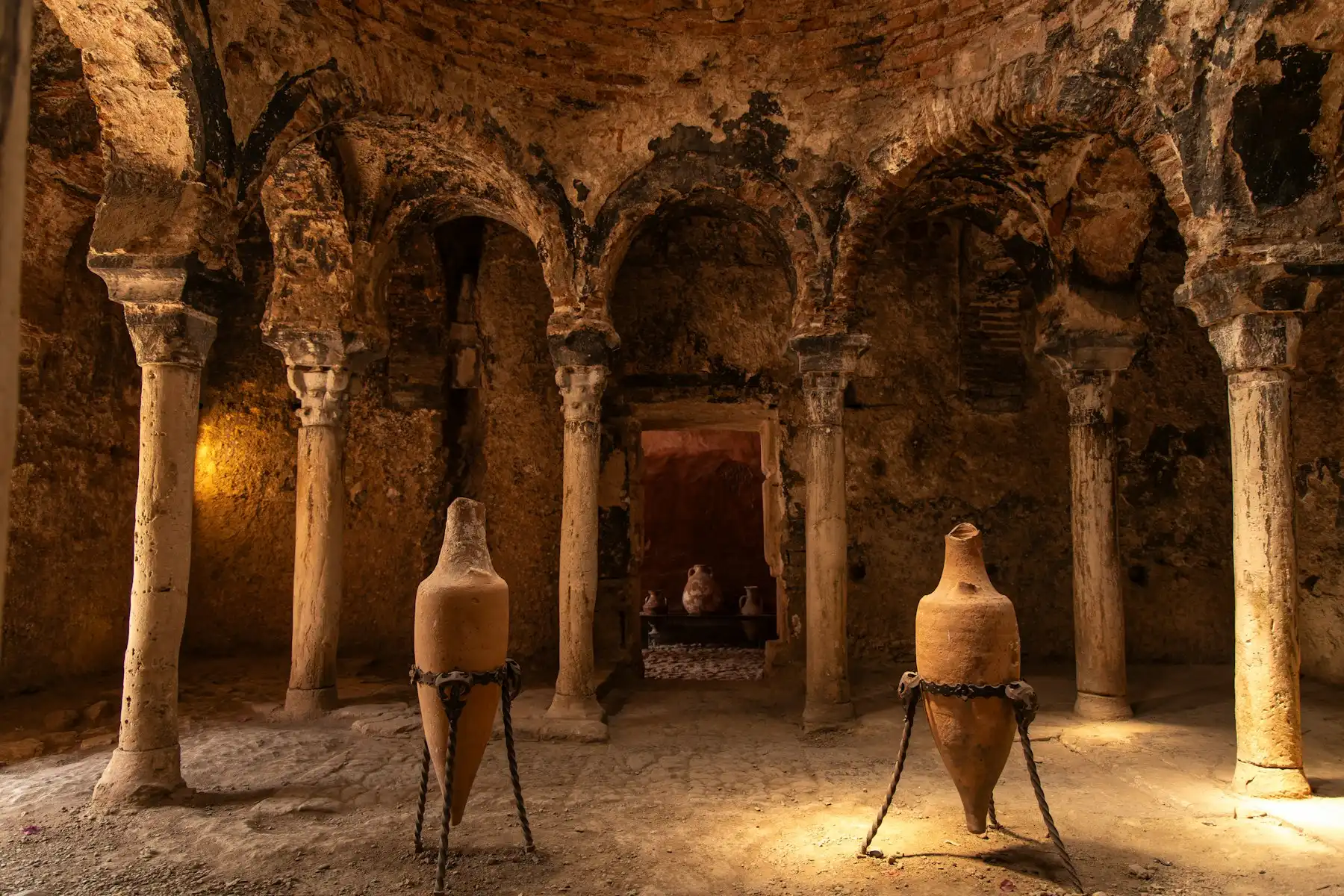 Ancient amphorae standing between carved stone columns in a lamplit vaulted chamber