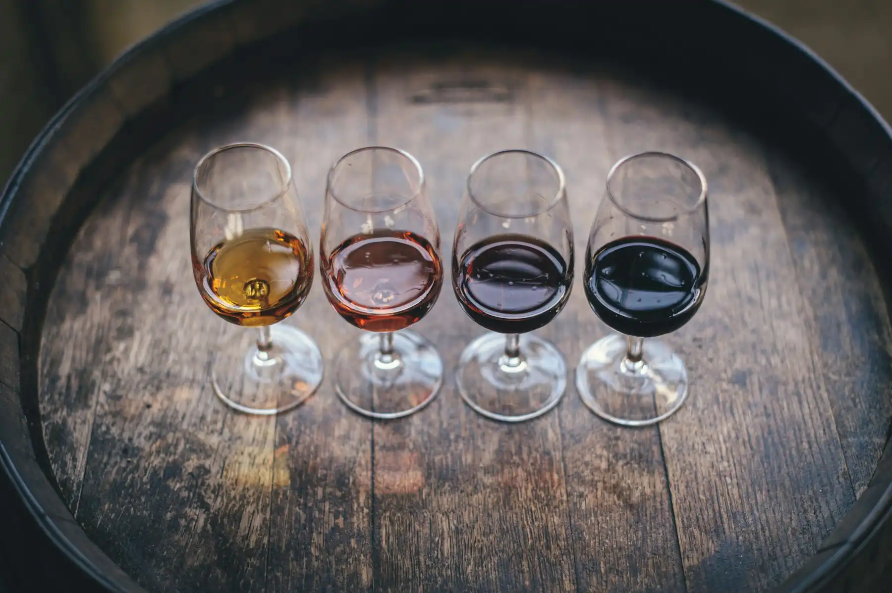A tasting flight of four wines — gold to deep red — lined up on a barrel head