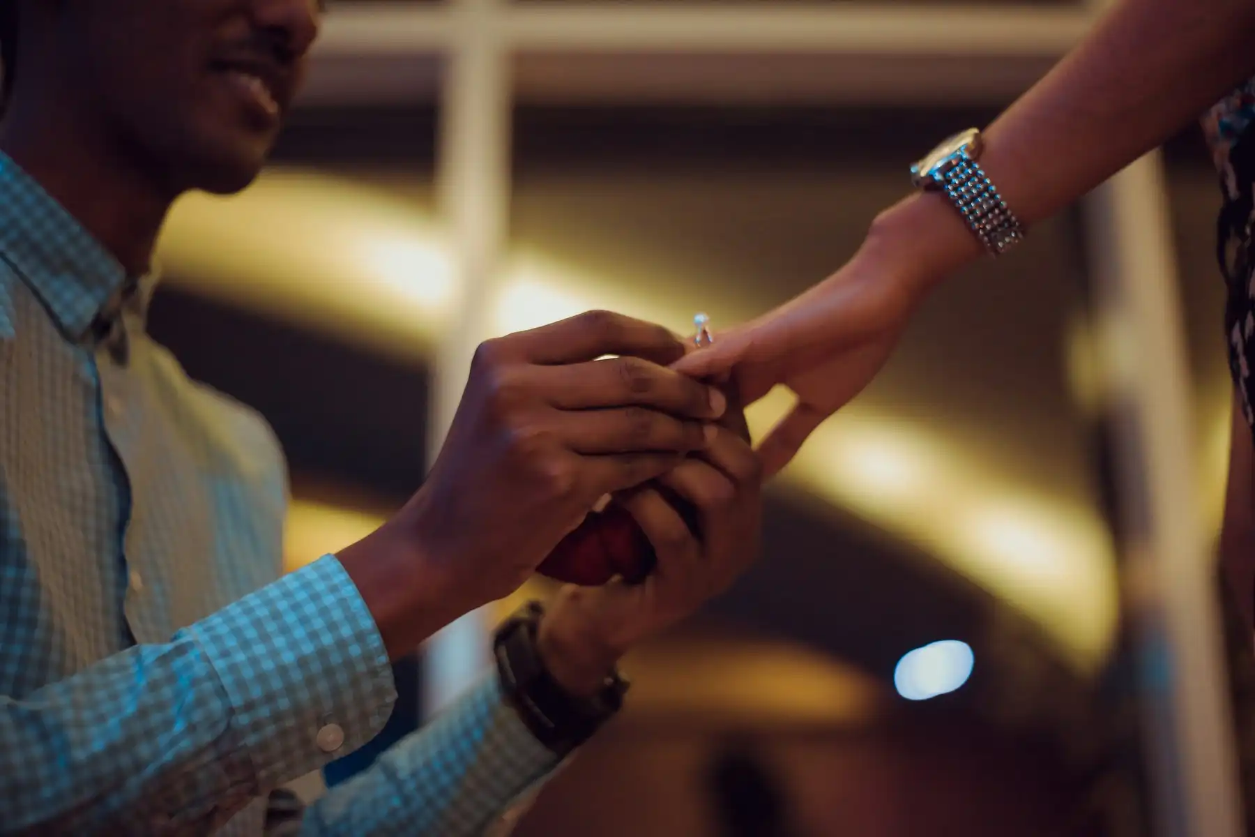 An engagement ring being slipped onto a partner’s finger in warm evening light