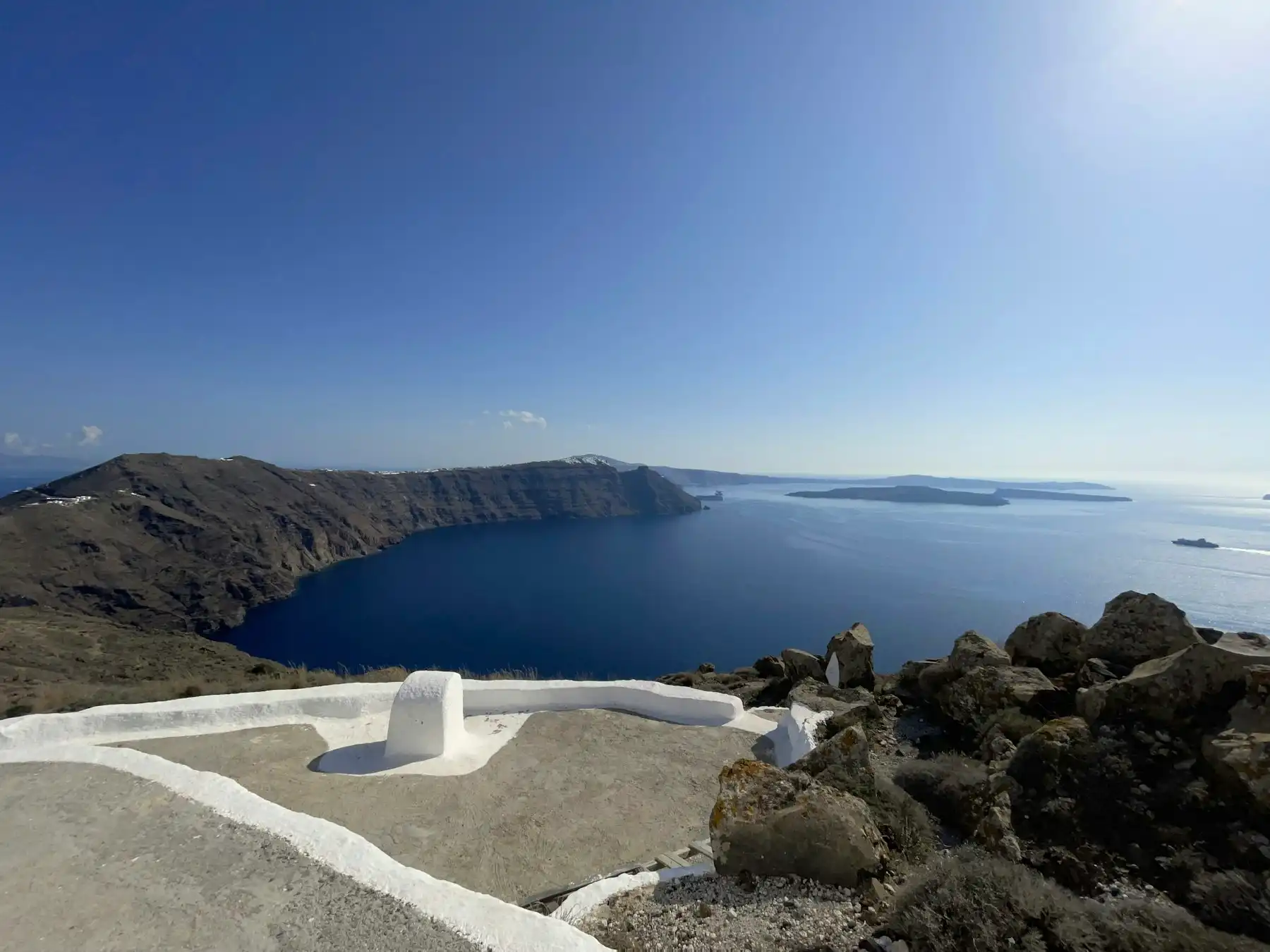 The caldera bowl from the rim path — a whitewashed chapel rooftop in the foreground and the sea filling the crater below
